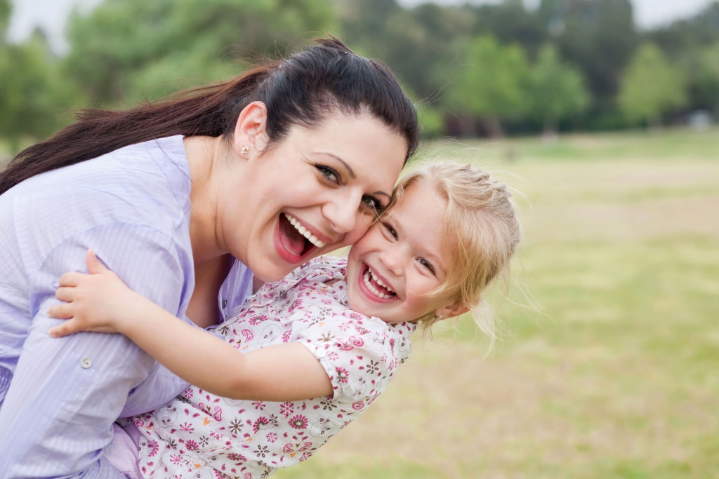 Happy mother carrying her daughter at the park
