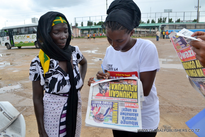 12.Mwanamama aitwae Maimuna Rashid (kushoto) akisaidiwa kujaza kuponi yake na muuzaji wa magazeti
